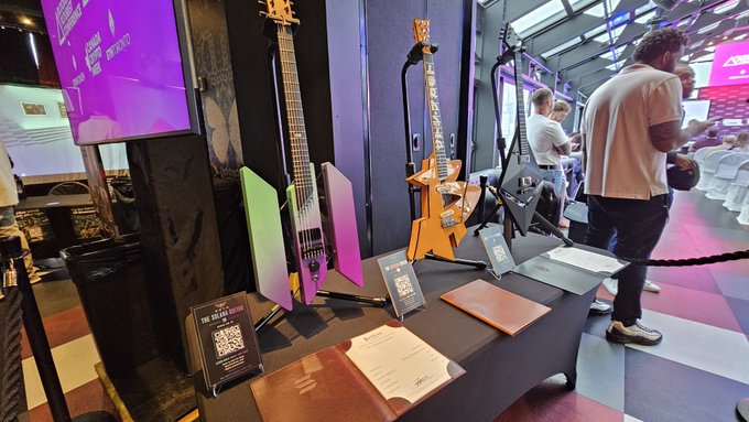 A music store or exhibition display featuring colorful electric guitars including a green/purple headless model and an orange angular design, with QR code placards on the table.