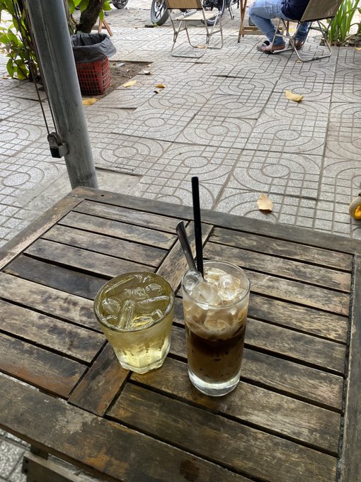 Two iced beverages served in glasses with black straws on an outdoor wooden table.