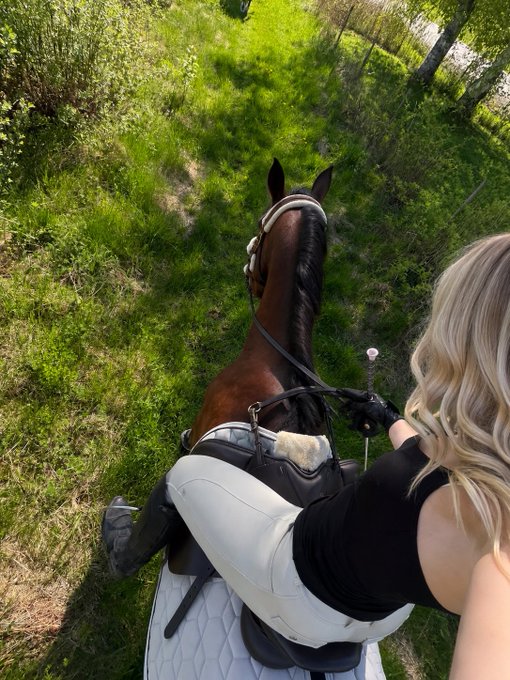 A rider with blonde hair sits atop a dark brown horse on a sunlit grassy trail, captured from a selfie angle. The image evokes a leisurely weekend vibe, complementing the post's cheerful "Happy Sunday" greeting and relaxed invitation for crypto conversation.