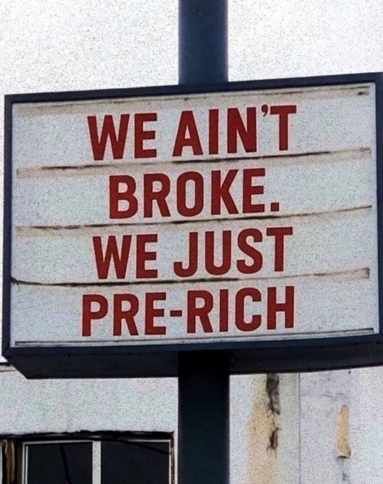 The image features a sign that reads "We Ain't Broke. We Just Pre-Rich", which has been edited with red text, giving it a humorous twist. The sign is attached to a pole outside of an office building or store, possibly indicating a sale or promotion related to the concept of being broke and pre-rich.