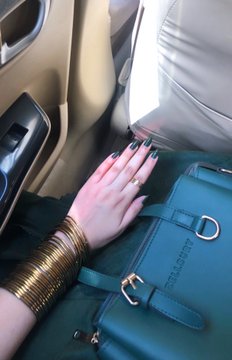 A hand with black manicured nails and a gold ring rests on a teal bag displaying the "BAGSMITH" logo inside a vehicle, accessorized with stacked gold bangles on the wrist. The image complements the post's reflective Independence Day message, suggesting a moment of pause and contemplation during a personal journey of exploring new opportunities like NFTs and ambassador programs.