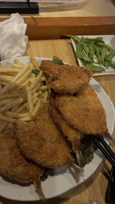 The image shows a plate of food, including fried fish sticks, french fries, and salad greens. The plate is placed on top of a dining table with various other plates and bowls around it. The photo appears to be taken during the day under natural light, creating an inviting atmosphere for enjoying this delicious meal.