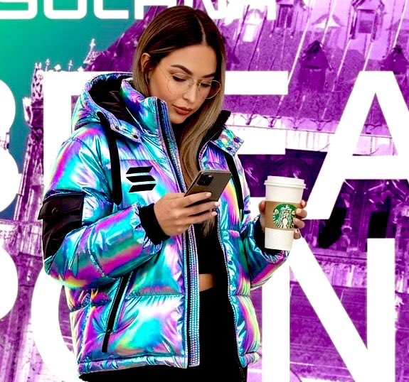 A stylized photo of a woman wearing a holographic iridescent puffer jacket, holding a smartphone and a Starbucks coffee cup, standing against a purple backdrop with 'SCARF' partially visible.