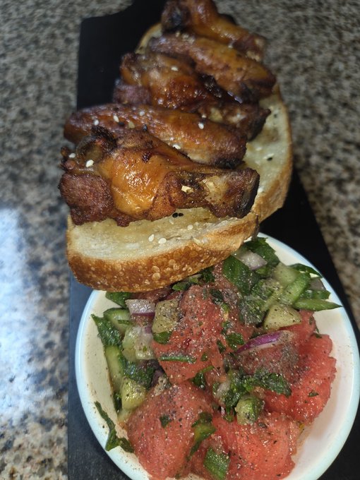 A delicious-looking meal features grilled meat skewers served over a slice of bread, placed next to a bowl of raw tuna tartare mixed with cucumbers and onions.