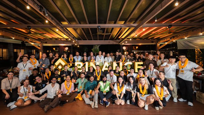 group photo of attendees at a Binance event, with the 'BINANCE' logo displayed.