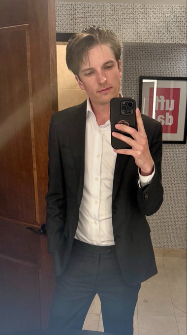 A man in a black blazer and white shirt takes a mirror selfie in a restroom, with an "ITU sb" sign visible on the tiled wall behind him. The polished professional look complements the post's announcement of his new role at BVNK Finance, where he's advancing stablecoin adoption for enterprises.