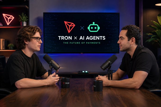 The image shows two men sitting at a table with microphones, appearing to be having a conversation or participating in an interview. The background features a large flat screen TV displaying information about blockchain technology and cryptocurrency. The text "TRON x AI Agents" is visible on the TV screen, which suggests that they are discussing the intersection of artificial intelligence (AI) and cryptocurrencies. This could potentially lead to discussions about the future of global payments or other applications of AI in the financial industry.