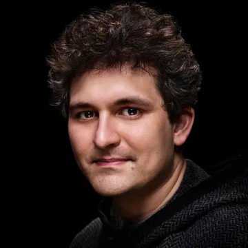A professional headshot portrait of a man with curly dark hair wearing a dark jacket against a black background.