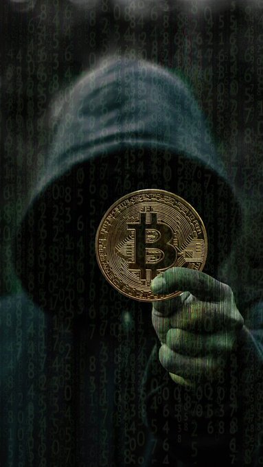 A person wearing a dark hoodie holds up a gold Bitcoin coin against a backdrop of a digital screen filled with falling green numbers, creating a hacker-like aesthetic.