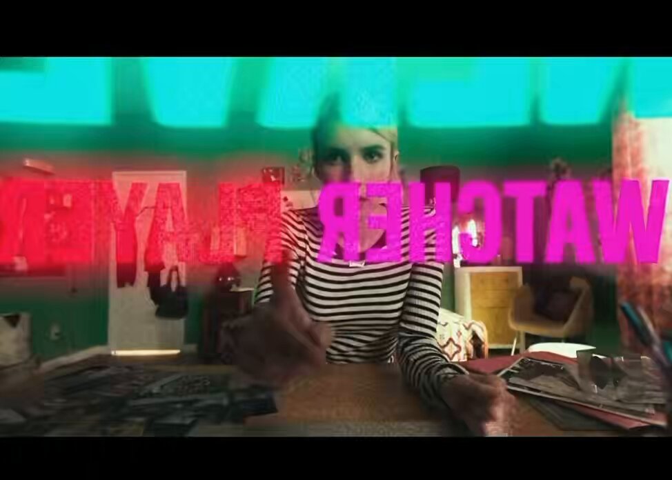 The image features a woman sitting at a table with her hands up, possibly giving a thumbs-up or making a gesture of approval. She appears to be wearing a striped shirt. In front of her are two books, which could indicate that she is participating in an online challenge related to reading or learning. The background shows a green door and a window, suggesting the setting might be indoors with some natural light coming through the window.