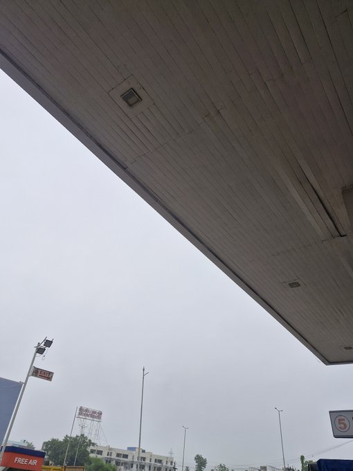 A view looking up at the underside of a large canopy or roof structure with a speed limit '5' sign visible, and a 'FREE AIR' sign at a gas station in the lower portion.
