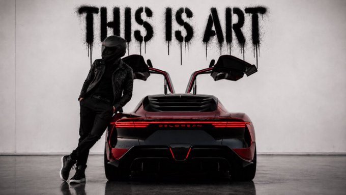 A person in a black helmet and jacket stands leaning against a red sports car with its doors open, positioned below the words "THIS IS ART" spray-painted on a white wall.