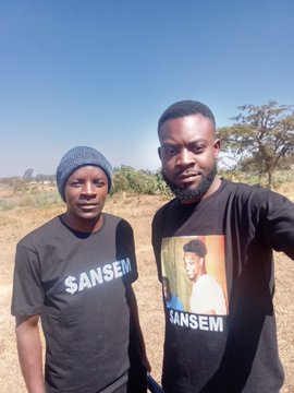 Two men wearing black 'SANSEM' branded t-shirts taking a selfie outdoors with a clear blue sky.