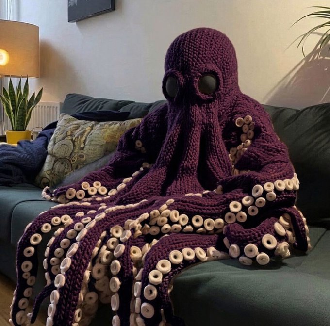 A purple crocheted octopus blanket with tentacles featuring cream-colored suction cup details draped over a dark green couch in a living room setting.