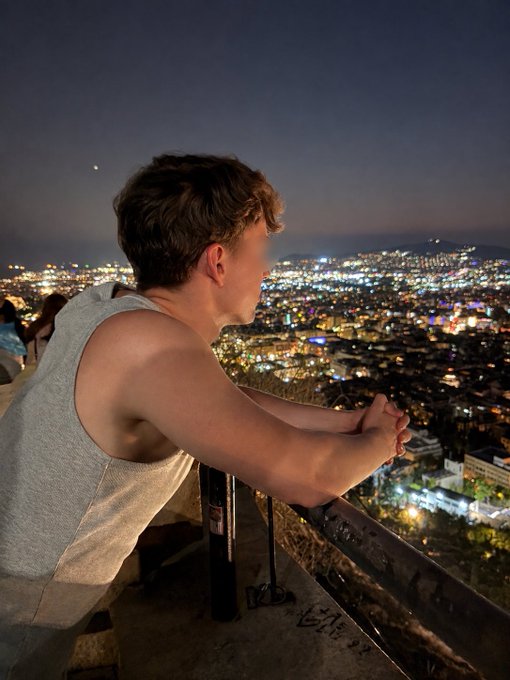 A young man in a gray tank top leans on a railing, gazing out over a sprawling city skyline illuminated at night. The image visually evokes the post's claim of "Solpump changed my life," suggesting a moment of reflection and newfound perspective from a high vantage point after personal transformation.