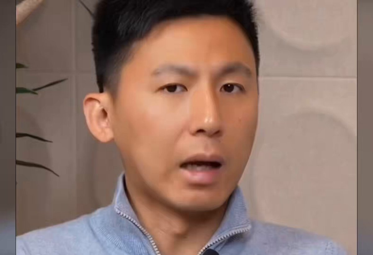 The image features a man with short black hair wearing a blue jacket, sitting next to a plant in his room. The focus of the photo seems to be more on the man rather than the background setting. There isn't any text accompanying the image that connects directly to the quote about cryptocurrency and its pricing patterns.