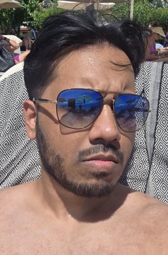 A man in blue reflective sunglasses relaxes poolside while his reflection reveals he's still checking his phone—capturing the irony of being on vacation but unable to stop thinking about making money.