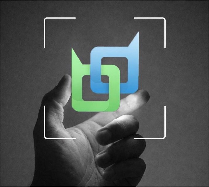 A black and white photograph of a hand holding up an interlocking green and blue chain link logo within a white camera viewfinder frame.