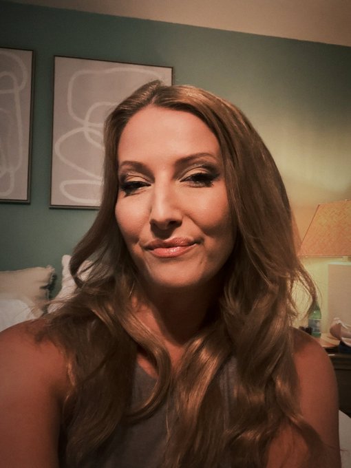 A woman with long, wavy brown hair smiles softly at the camera in a warmly lit room with framed artwork behind her. The image accompanies her birthday post, where she celebrates turning 44 while sharing wishes that include promoting the @UseArtisan waitlist.