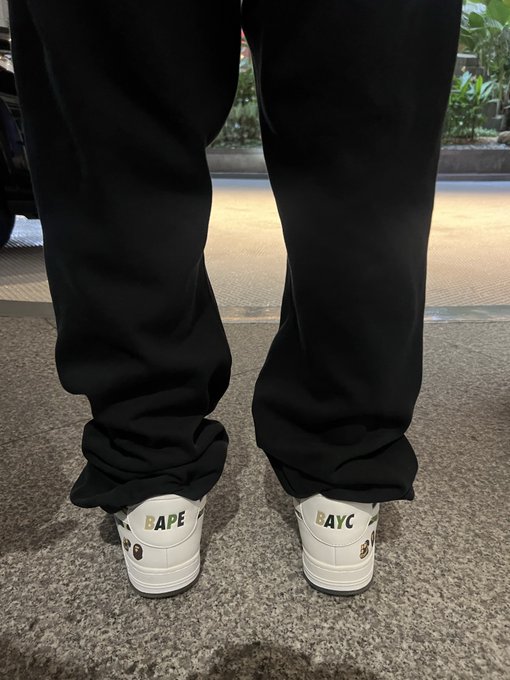 A person wearing black pants and white sneakers with "BAPE" on the left shoe and "BAYC" on the right, matching the post's reference to the Bored Ape Yacht Club.