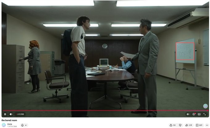The image shows a group of people standing around a table, with one person holding a remote control. The scene appears to be set in an office environment where they are gathered for a meeting or discussion. A whiteboard can also be seen on the wall behind them, indicating that this is likely a professional setting.