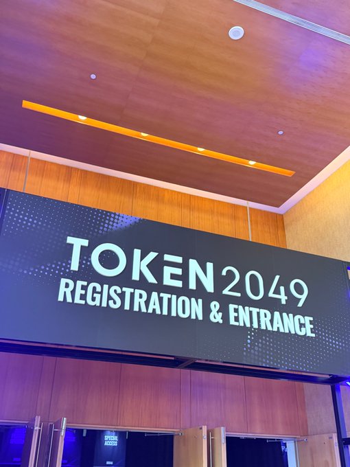 The image shows an illuminated "TOKEN 2049 REGISTRATION & ENTRANCE" sign hanging in a venue lobby, marking the entry point to the TOKEN2049 cryptocurrency conference. The excited caption "TOOOOOOOKEN2049" reflects the blogger's enthusiastic arrival at the event.