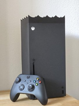 A black Xbox Series X console stands vertically on a wooden surface, with a black wireless controller placed in front of it.