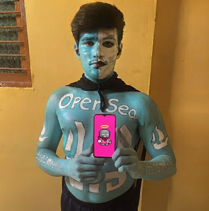 A man covered in body art featuring "Open Sea" text holds up a phone displaying a pixel character, promoting the upcoming launch of "Mini Brokers" on OpenSea as teased in the post.
