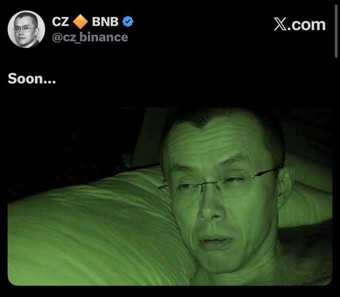 A tweet from CZ 🔶 BNB (@cz_binance) featuring a green-tinted photo of himself in bed with the caption 'Soon...'
