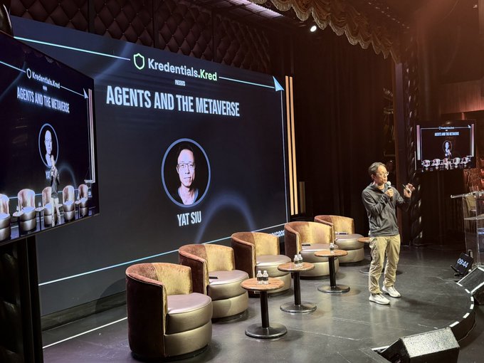 A stage presentation titled 'Kredentials.Kred - AGENTS AND THE METAVERSE' featuring a speaker named Yat Siu, with empty chairs arranged in front of a large screen.