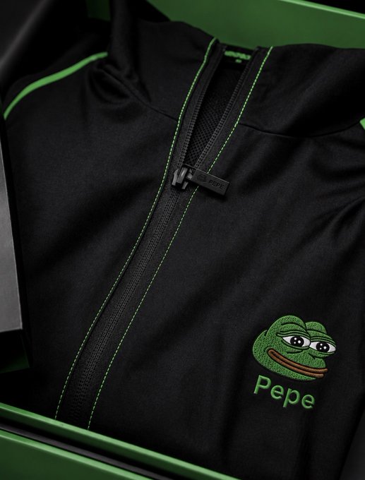 A close-up of a black Pepe the Frog branded zip-up jacket with green stitching and an embroidered logo with the name "Pepe."