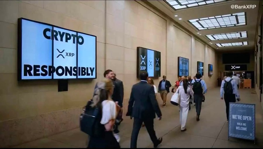 Photo of a conference hallway with attendees walking past illuminated signs reading 'CRYPTO XRP RESPONSIBLY,' watermarked with '@BankXRP.'