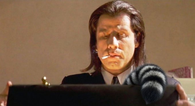 A long-haired man in a suit with a cigarette in his mouth holds an open briefcase containing a raccoon in what appears to be a scene from the film "Pulp Fiction."