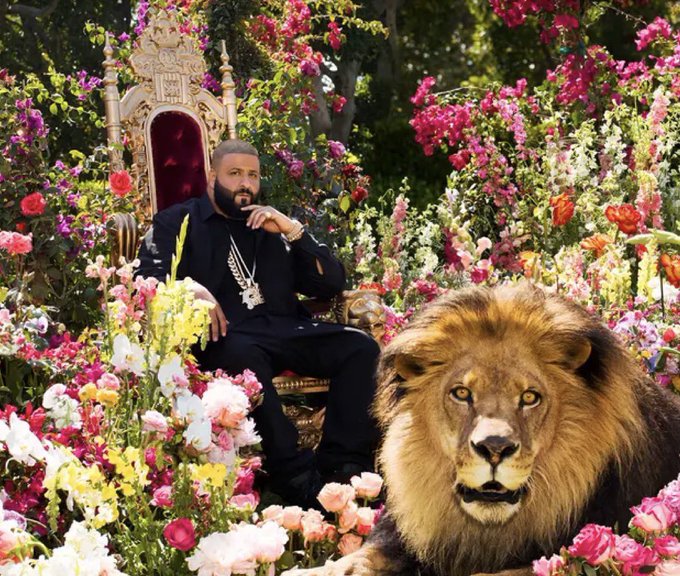 The album cover for DJ Khaled's music features him seated on a golden throne surrounded by a lush garden of colorful flowers, wearing all black with gold chains, with a large male lion resting in the foreground.