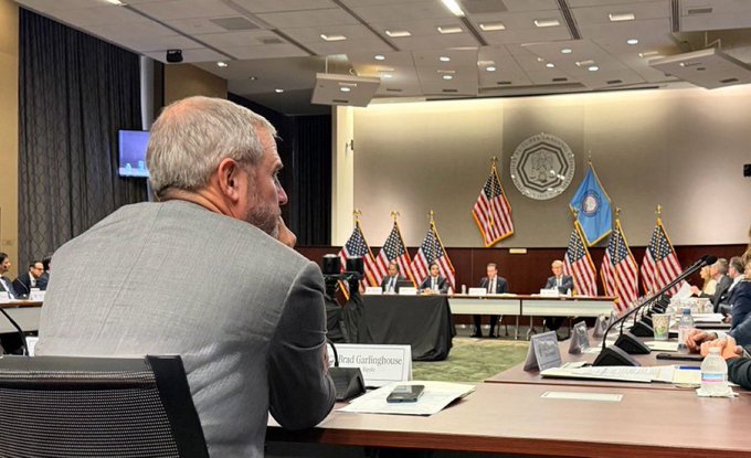 Ripple CEO Brad Garlinghouse, identified by his name placard, is seen seated at this week's CFTC meeting, with American flags and the CFTC seal displayed prominently behind the panel of officials, suggesting the regulatory discussion ties into the post's message that "we've never been closer" to crypto regulatory clarity.