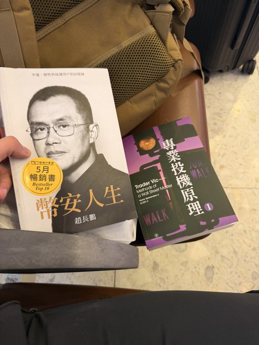 The image shows two Chinese books—one titled "幣安人生" (Binance Life) by 趙長鵬 (CZ), with a note that it's a 5-month bestseller, and another titled "專業投機原理" (Trader Vic: Methods of a Wall Street Master). This pairs with the post's joke about being randomly checked at Chinese customs and proudly declaring "Binance Life" as the reason for carrying the books, poking fun at fellow crypto enthusiasts.