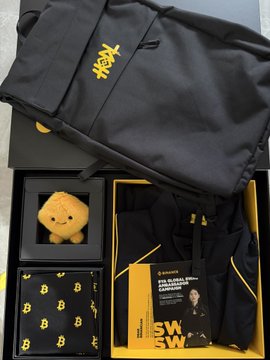 The image displays a Binance 9th Anniversary gift package, including a black tote bag with the yellow Binance logo, a BNB (Binance Coin) stress ball, a "9 years" themed cloth, and a "$W Web3 Wallet Card" featuring a person in formal attire, all arranged in a presentation box. This collection of branded merchandise celebrates Binance's nine-year journey from its 2017 launch and BNB issuance to becoming a global crypto exchange leader.