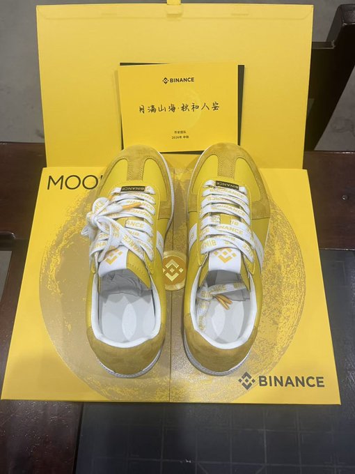 A pair of yellow and white sneakers with Binance branding sit atop a yellow Binance-themed box alongside a card reading "BINANCE 月满山海 秋和入笙 2024中秋" (Moon over mountains and seas, autumn brings peace), serving as a Mid-Autumn Festival gift from Binance.