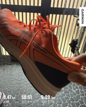A close-up of an orange Nike racing shoe held up to the camera, with a Garmin watch display in the bottom corner showing a run distance of 8.47 km in 50:51 at a 6:00 km/m pace.