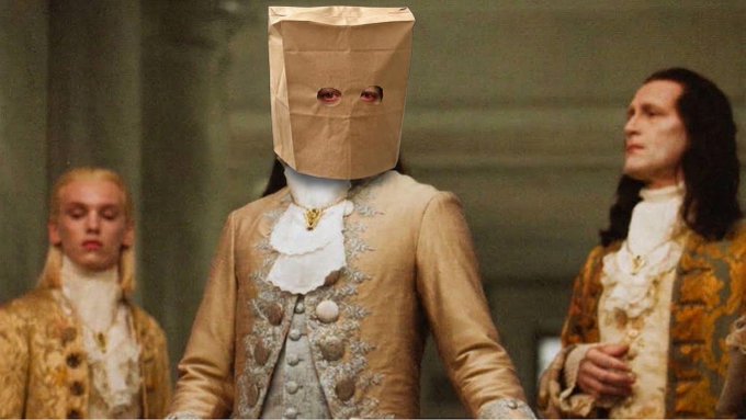 A person in an ornate gold 18th-century coat has a brown paper bag over their head with eye holes cut out, flanked by two similarly dressed figures.