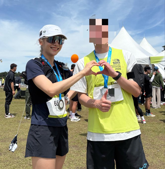 Two runners pose together at what appears to be a running event, forming a heart shape with their hands to celebrate their accomplishment, with one wearing bib number 65 and the other wearing a bib that reads "THE NORTH FACE 100 NGWON 2025." The gesture of creating a heart with their hands directly reflects the accompanying caption "The Heart and Me," symbolizing a personal connection and shared passion for the sport.