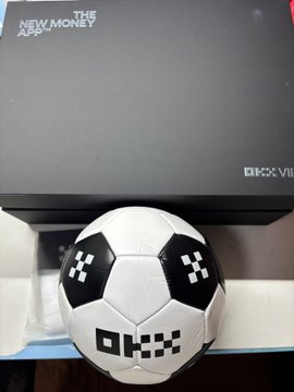 A black OKX "The New Apple of Money" gift box sits behind a soccer ball, matching the VIP-themed delivery reveal in the caption.