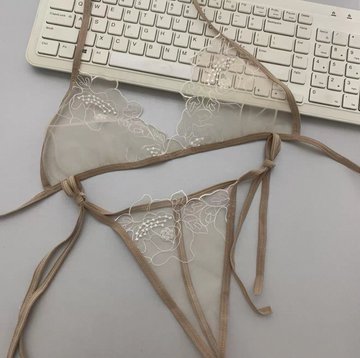 A beige sheer lace lingerie set laid out on a white keyboard.