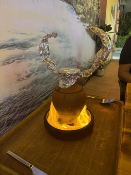 A silver metallic crescent-shaped decorative object displayed on a glowing warm-lit base in front of a wall mural.