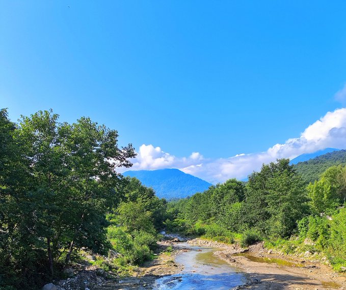 A serene mountain landscape with a flowing river, lush greenery, and a bright blue sky sets a peaceful morning tone, complementing the post's message about starting the week fresh and embracing consistent, mindful habits.