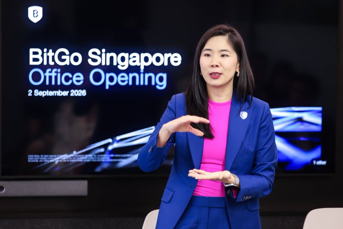 A woman in a blue suit with a pink top gestures while speaking at an event, with a screen behind her displaying "BitGo Singapore Office Opening - 2 September 2026." The image captures the official unveiling of BitGo's new Singapore office, which has tripled its APAC client base and doubled its Singapore headcount following its MAS Major Payment Institution licence.