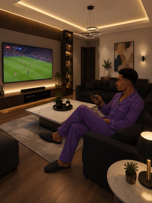 A man in purple pajamas sits in a modern living room holding a remote, watching a soccer match displayed on a large wall-mounted TV.