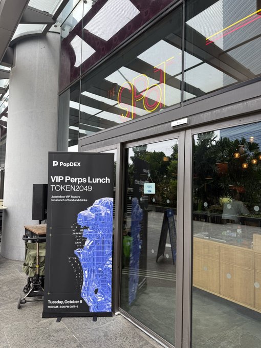 An entrance to a venue with a 'THE SPOT' neon sign above the door, featuring a PopDEX banner advertising a 'VIP Perps Lunch' for TOKEN2049 on Tuesday, October 8, 2024.
