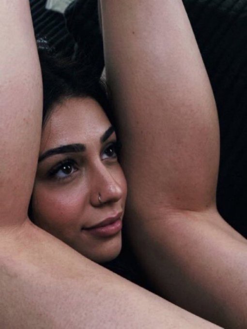 A young woman with a nose ring gazes seductively toward the camera, her arms raised and crossed behind her head in a sultry pose. The intimate, relaxed expression captures the lingering thrill and lingering tension of a copy trader who just watched Remus bid a coin on FOMO—equal parts excitement and quiet reflection on the risky move.