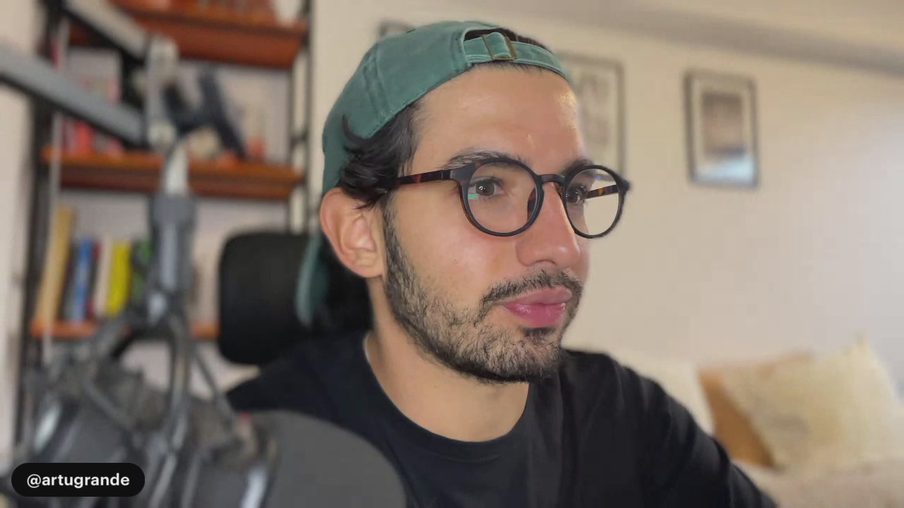 The image features a man wearing glasses and a hat sitting down with his eyes closed. He appears to be taking a break or relaxing during work. The background of the image shows a bookshelf filled with various books, suggesting that Artu is an individual who enjoys reading and learning about different subjects.